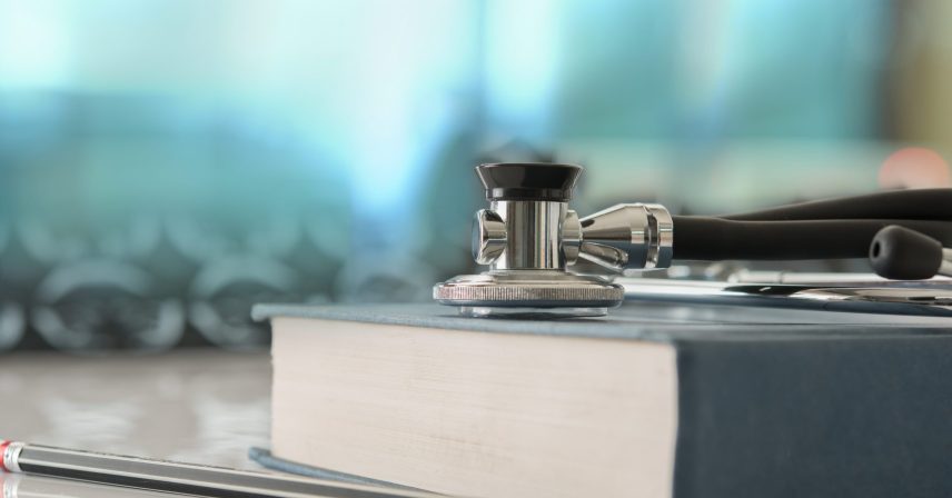 healthcare and medicine concept. Stethoscope with medical text book on doctor student desk at classroom in the hospital.